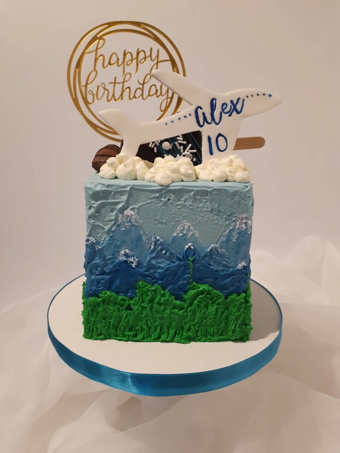 Blue airplane birthday cake with mountains and grass