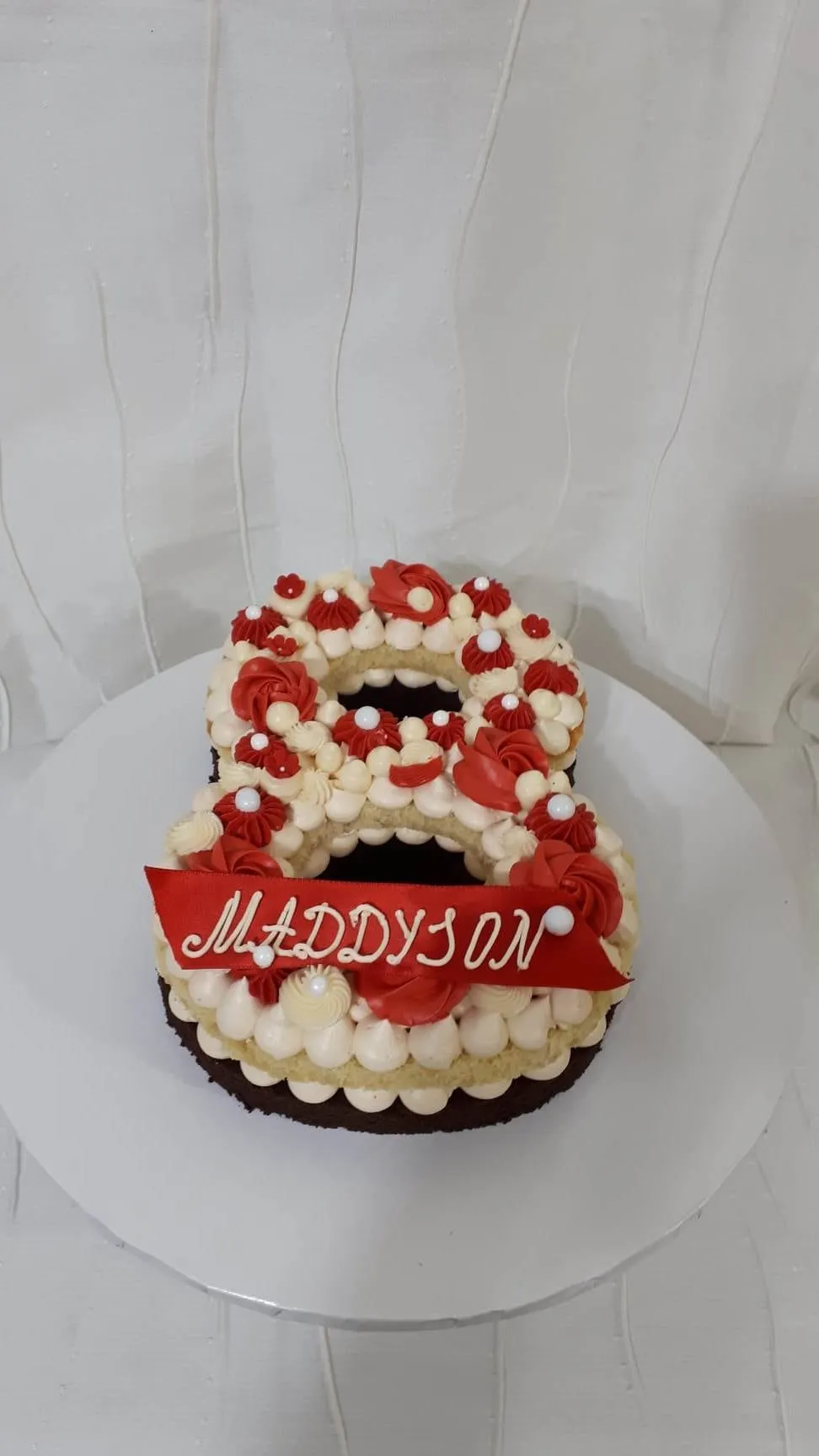 Number 8 cake with red and cream rosettes, pearls and a red name banner