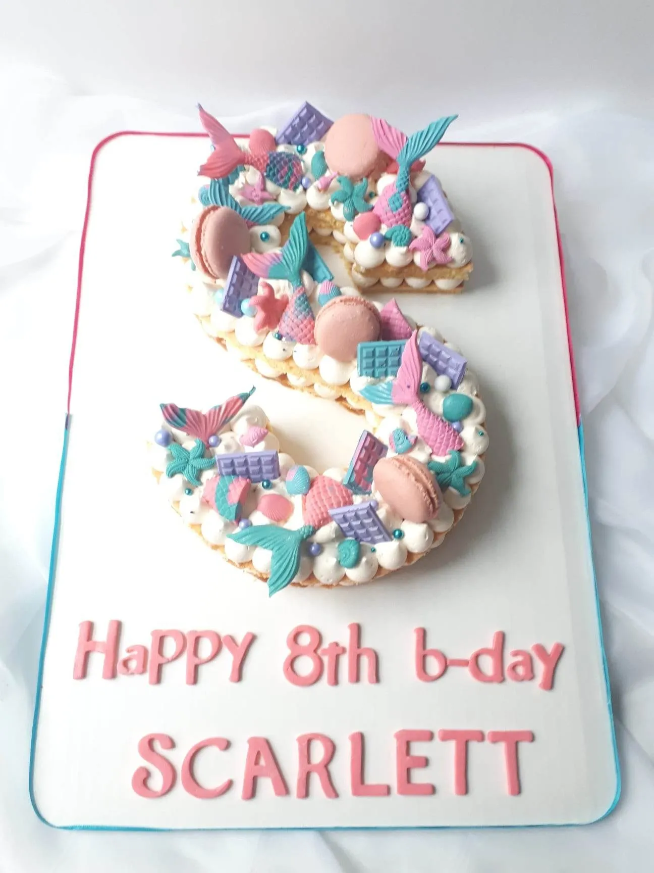 Letter S cake topped with mermaid tails, seashells and pastel macarons