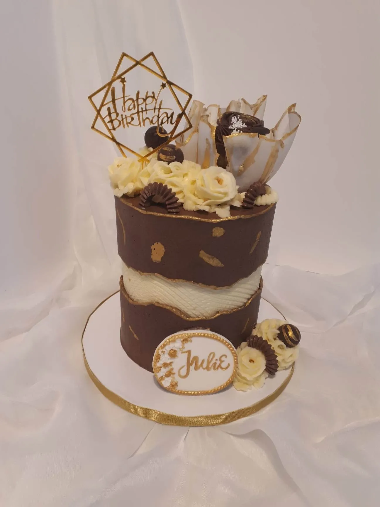 Tall brown and gold birthday cake with cream flowers